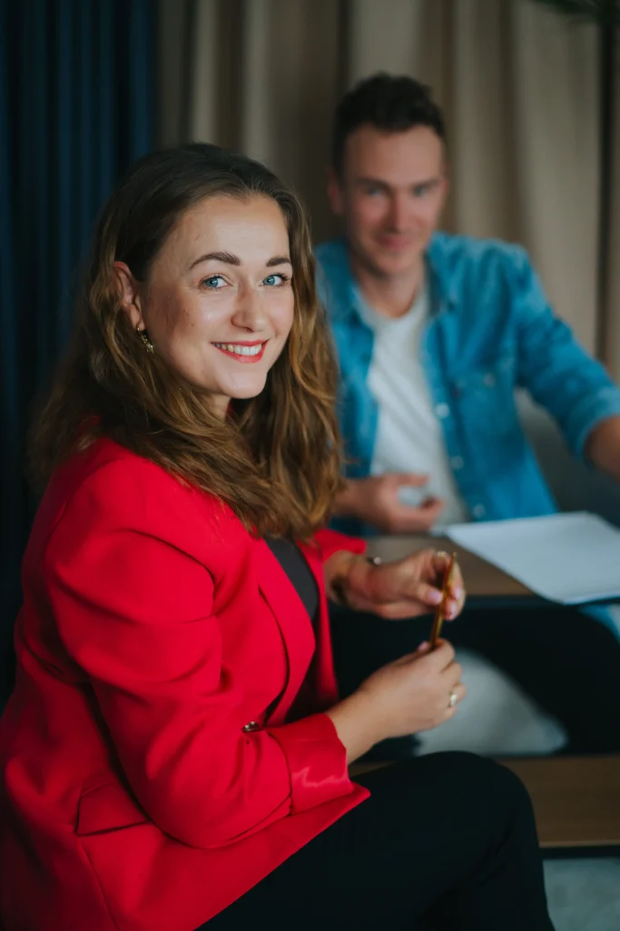 Kobieta w czerwonej marynarce uśmiecha się przy biurku podczas spotkania marketingowego.