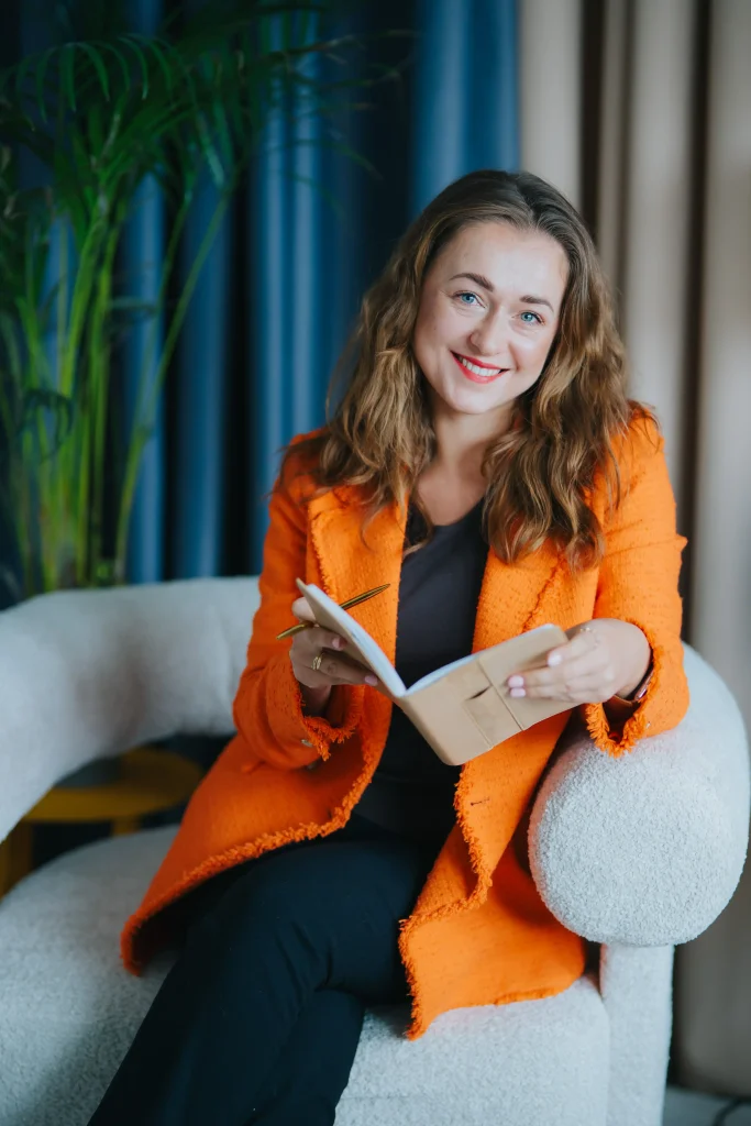 Osoba w pomarańczowej marynarce z notatnikiem, symbol profesjonalizmu w marketingu internetowym.