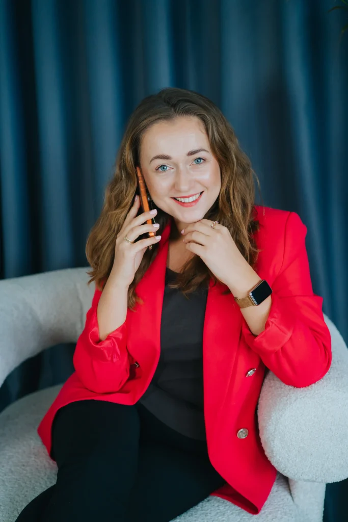 Kobieta w czerwonej marynarce siedzi i rozmawia przez telefon, uśmiechając się, marketing internetowy.