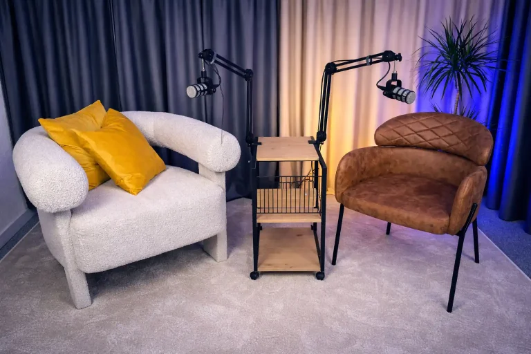 Pomieszczenie do podcastu z mikrofonami, białym i brązowym fotelem, gotowe do nagrań marketingowych.