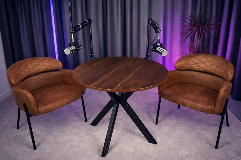 Stół konferencyjny z dwoma mikrofonami i brązowymi fotelami w studio marketingu Ambitna Marka.